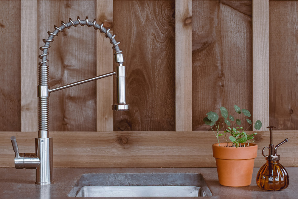 a kitchen counter and sink with a commercial style faucet and wood backsplash